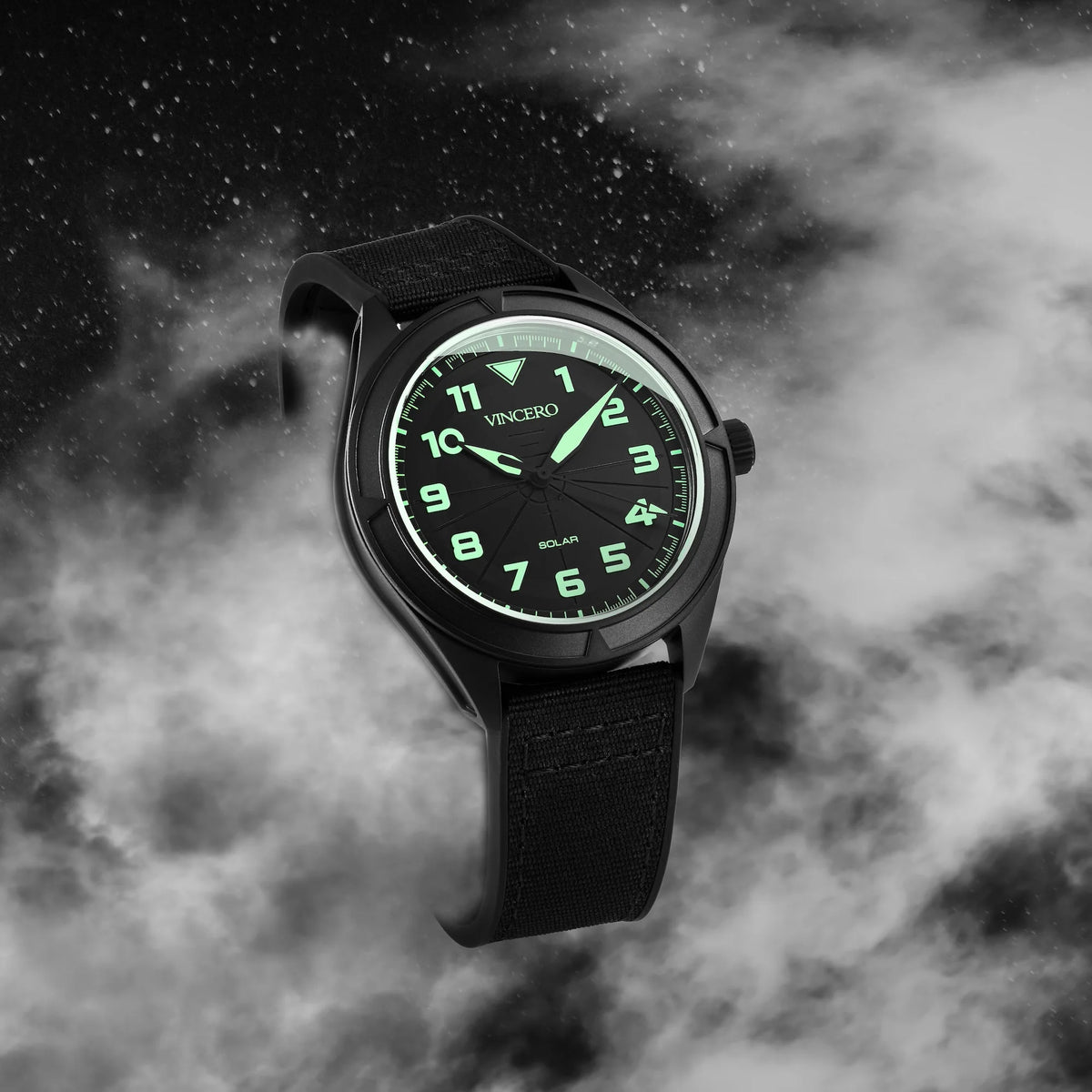 Black wristwatch with green glowing face on a dark, cloud-like background