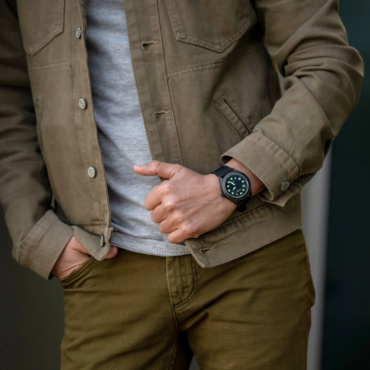 Person wearing a brown jacket and pants with a watch on a dark background