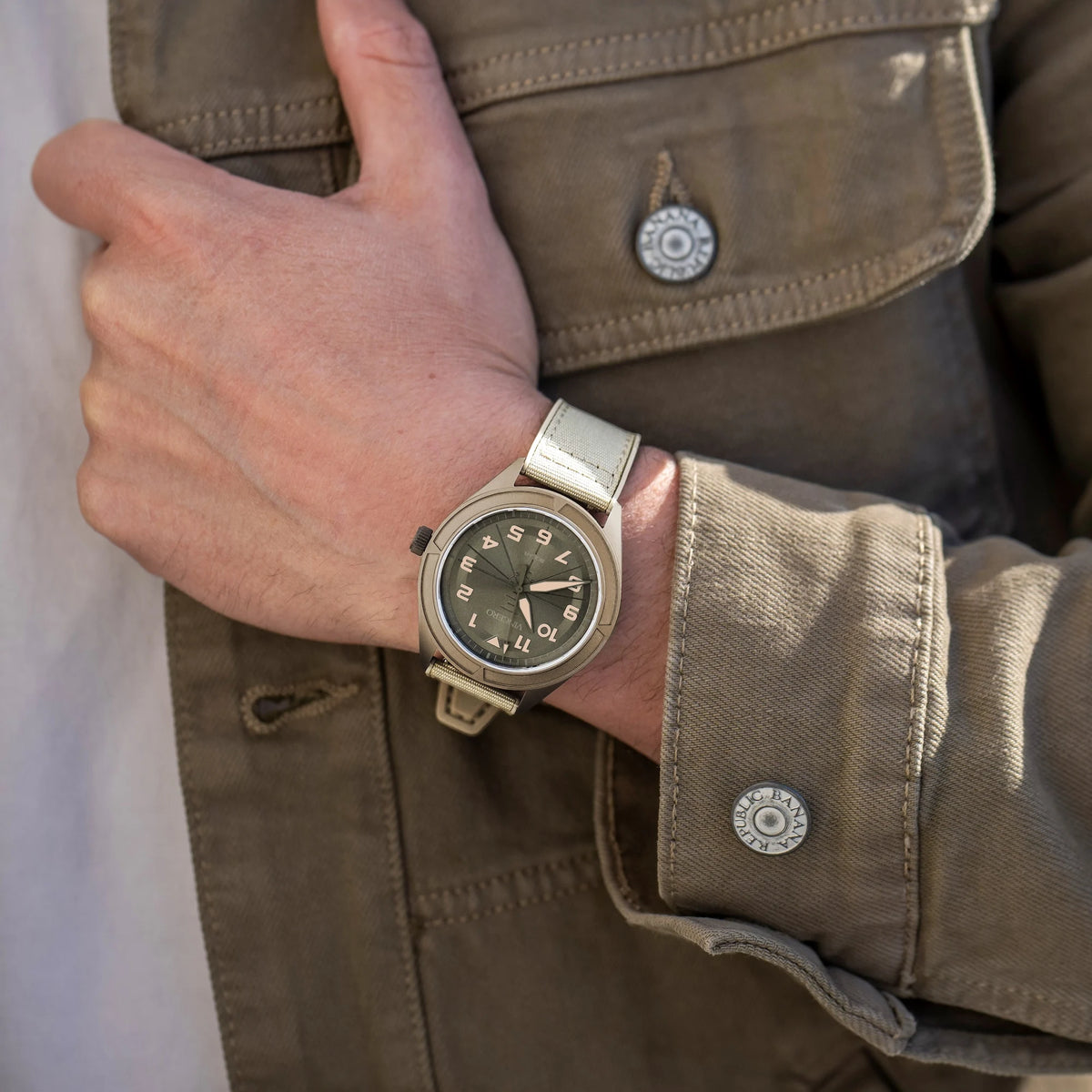 Hand wearing a watch with a brown jacket