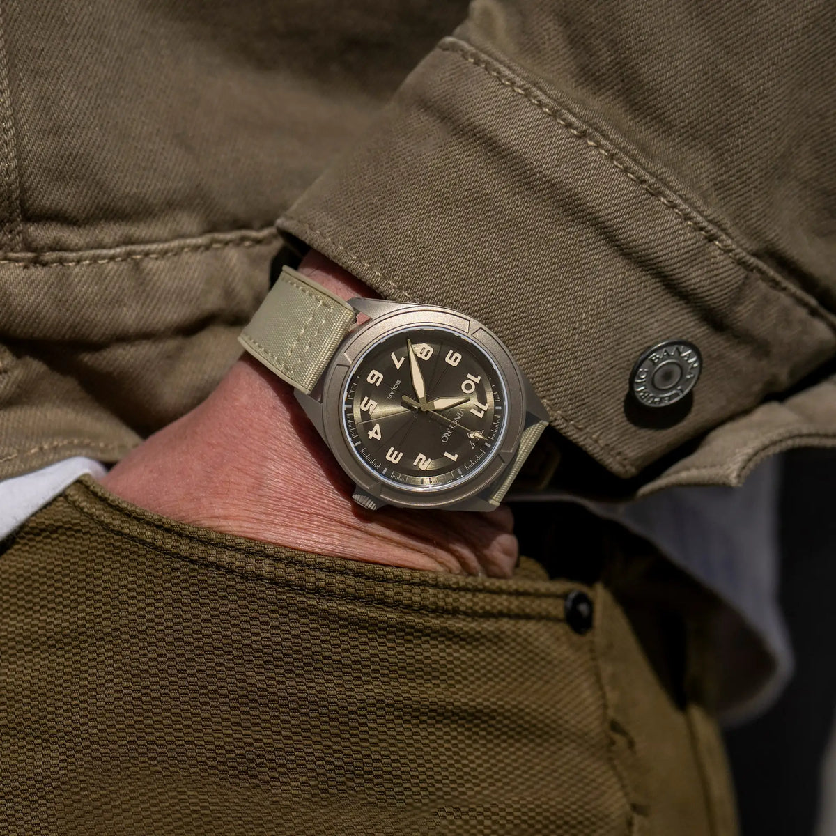 Close-up of a wrist wearing a watch with a brown leather strap, set against a brown jacket.
