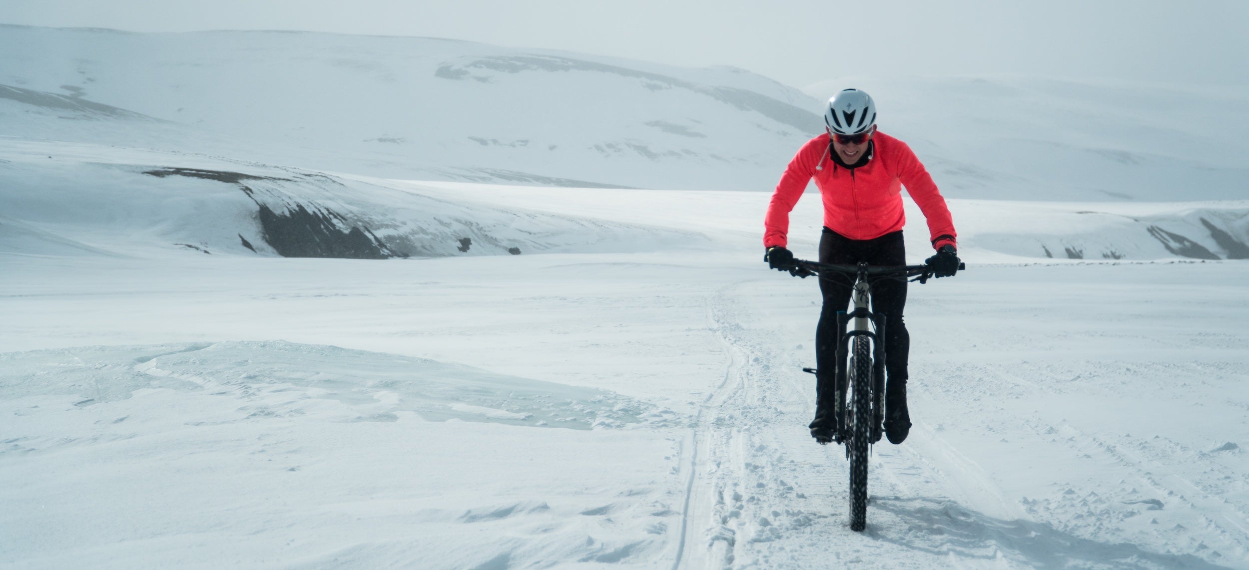 Man biking in winter conditions, with snow-covered land and mountains in the background.
