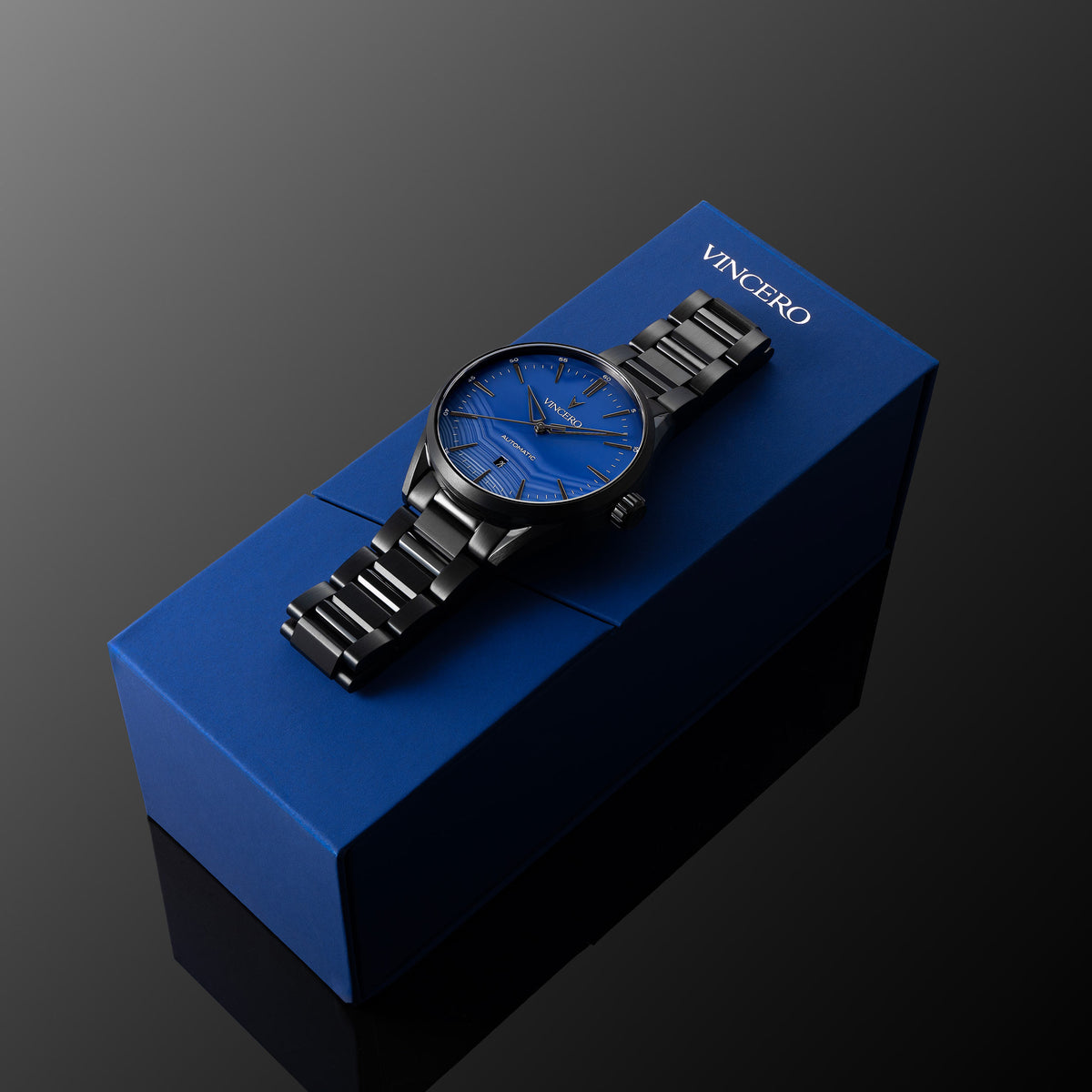 Black wristwatch with blue dial on a blue Vancero box against a dark background