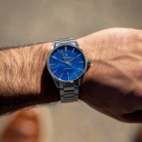 Silver watch with a blue face on a wrist against a blurred background