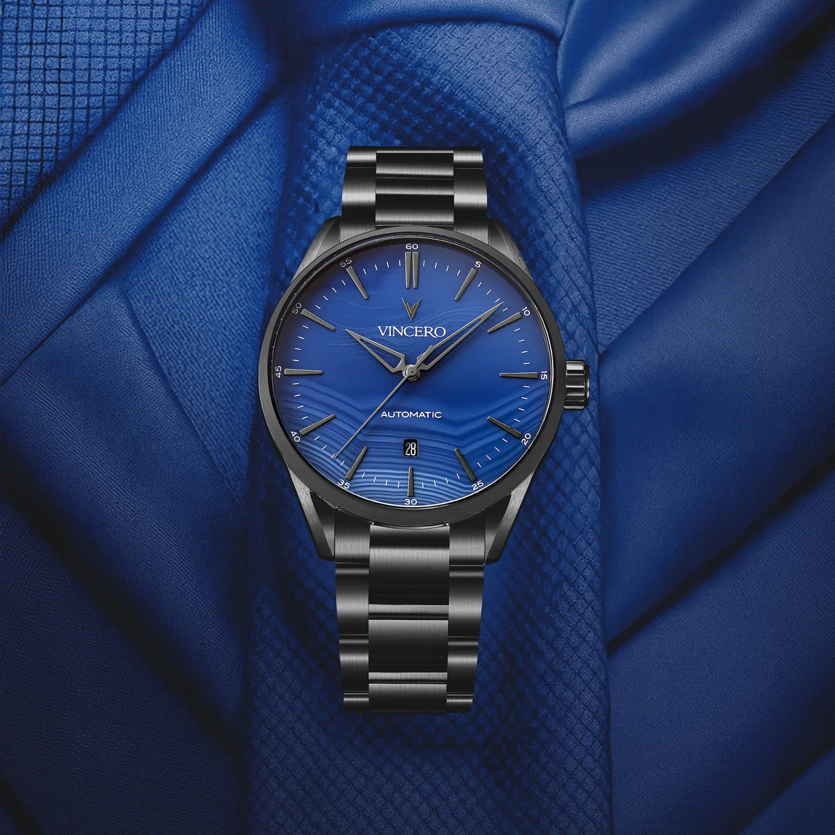 Vincero watch with blue dial and black bracelet on a blue fabric background