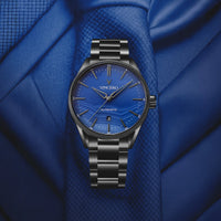 Vincero watch with blue dial and black bracelet on a blue fabric background