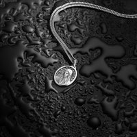 Silver necklace with a pendant on a textured black surface