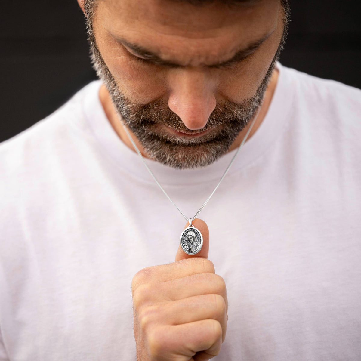 Man wearing a necklace with a pendant, looking down.