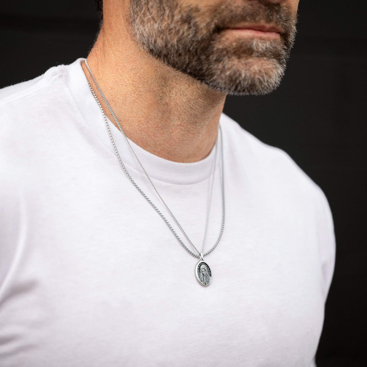 Man wearing a silver necklace with a pendant on a black background