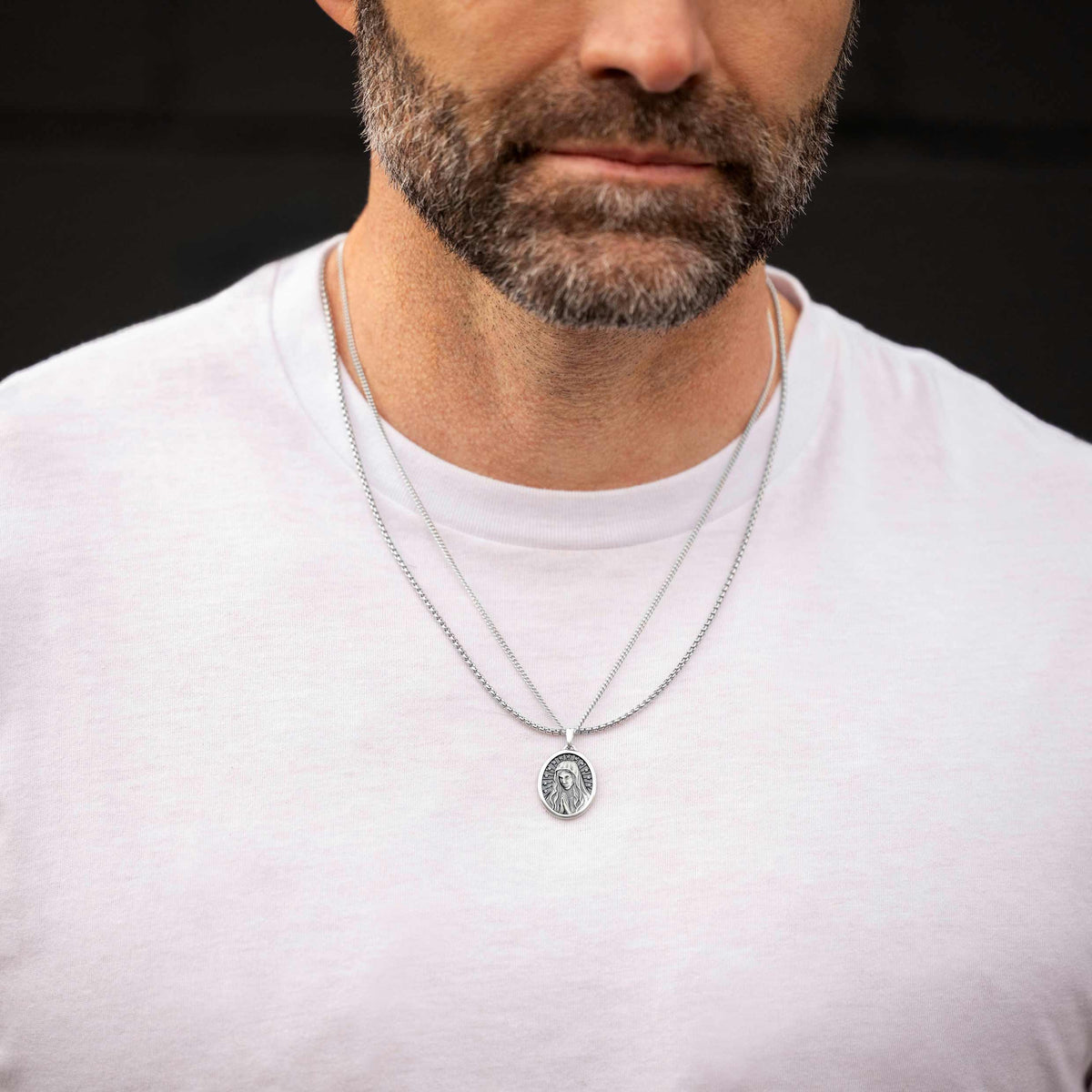 Man wearing a silver necklace with a pendant on a dark background