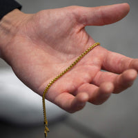 Gold chain held in a hand against a neutral background