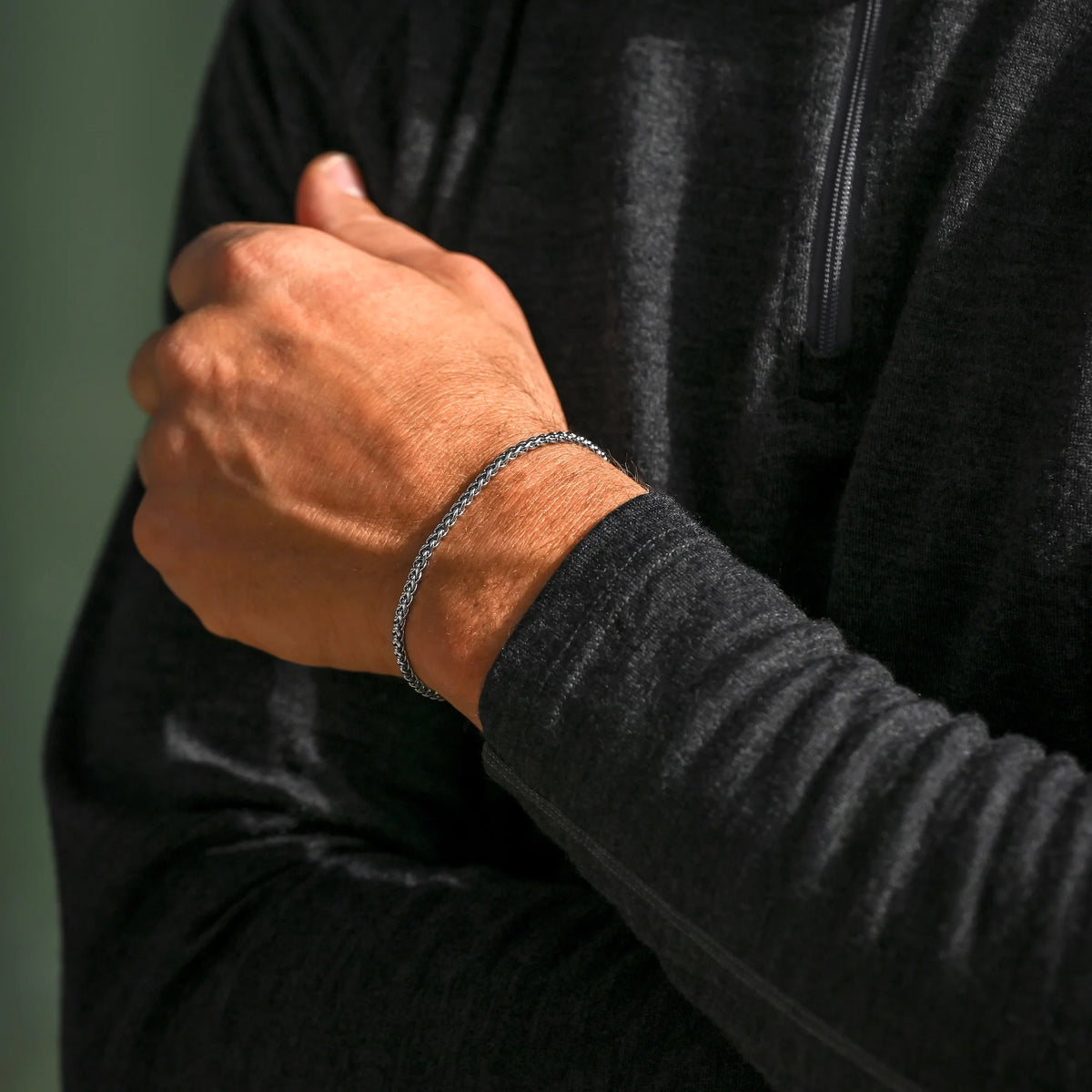 Person wearing a black hoodie with a focus on a bracelet on a green background
