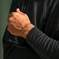 Person wearing a black hoodie with a focus on a bracelet on a green background