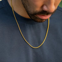 Gold chain necklace worn by a person on a dark blue shirt