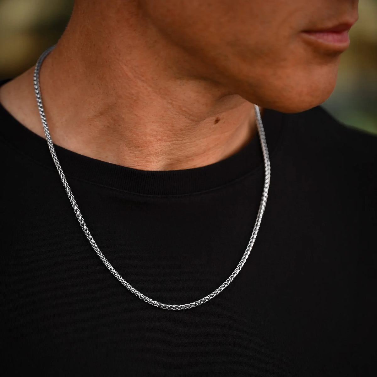 Person wearing a silver chain necklace against a blurred background