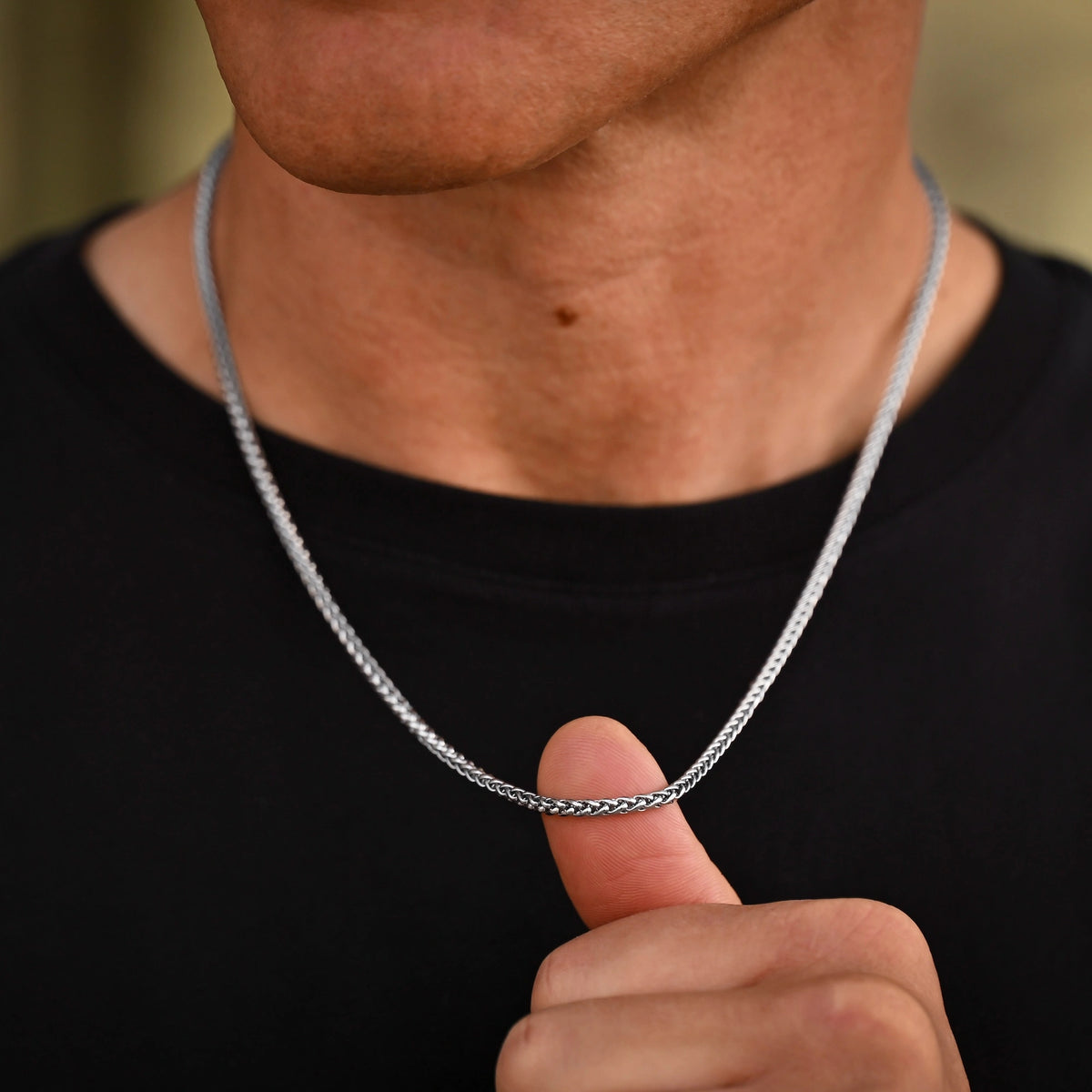 Person holding a silver chain necklace against a black background