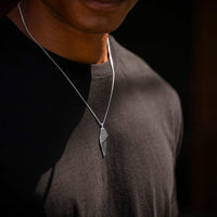 Person wearing a necklace with a leaf-shaped pendant on a dark background