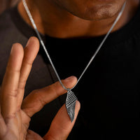 Silver necklace with a wing-shaped pendant held by a hand against a dark background