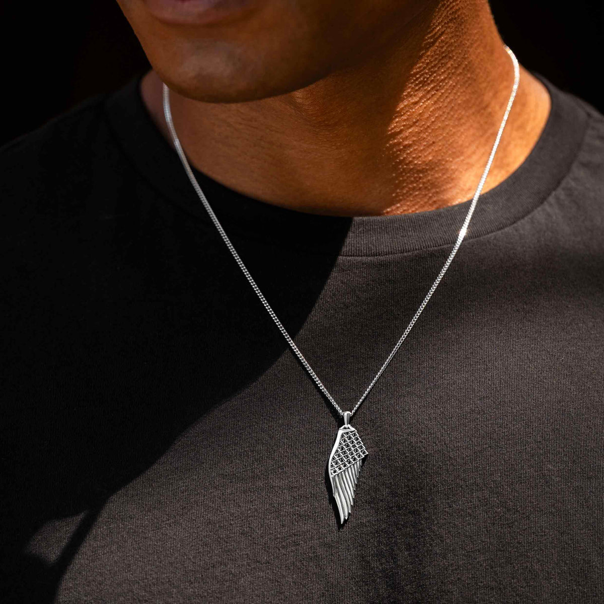 Silver wing-shaped pendant necklace on a person wearing a black shirt.