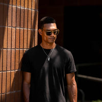 Man wearing sunglasses and a black shirt leaning against a brick wall.