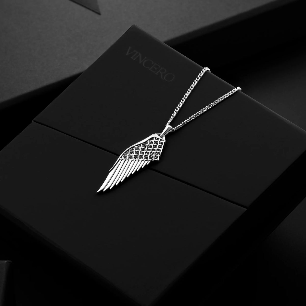 Silver wing-shaped necklace on a black box with 'Vincero' branding.