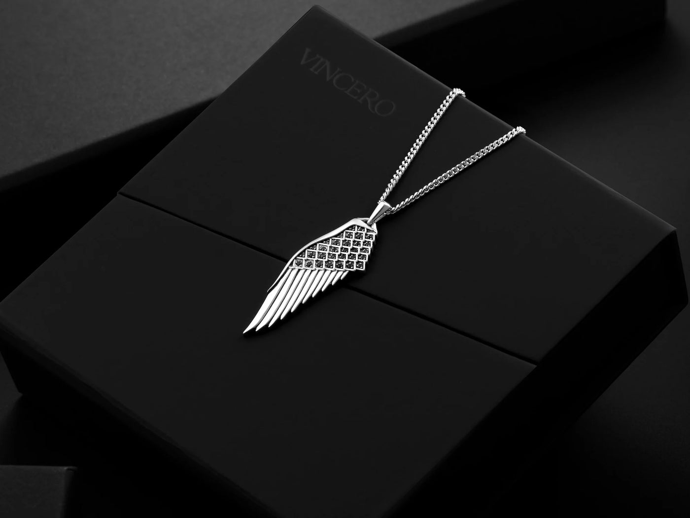 Silver wing-shaped pendant on a black box with 'VINCERO' branding.
