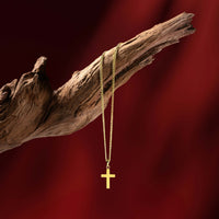 Gold necklace with a cross pendant on a wooden branch against a red background