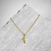 Gold cross necklace on a textured gray surface
