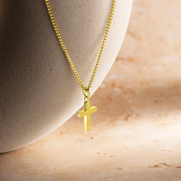 Gold cross necklace on a neutral background