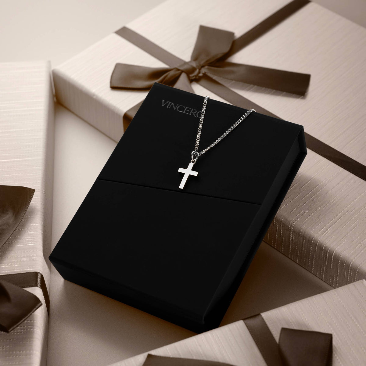 Silver cross necklace on a black box with 'Vincero' branding, surrounded by gift boxes.