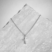 Silver cross necklace on a textured gray surface