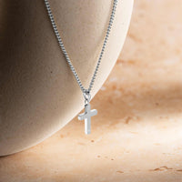 Silver cross necklace on a person's neck against a neutral background
