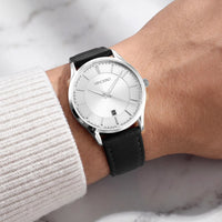 A Vincero wristwatch with a silver dial and a black leather strap, shown worn on a person's wrist with a white ribbed sweater sleeve visible.