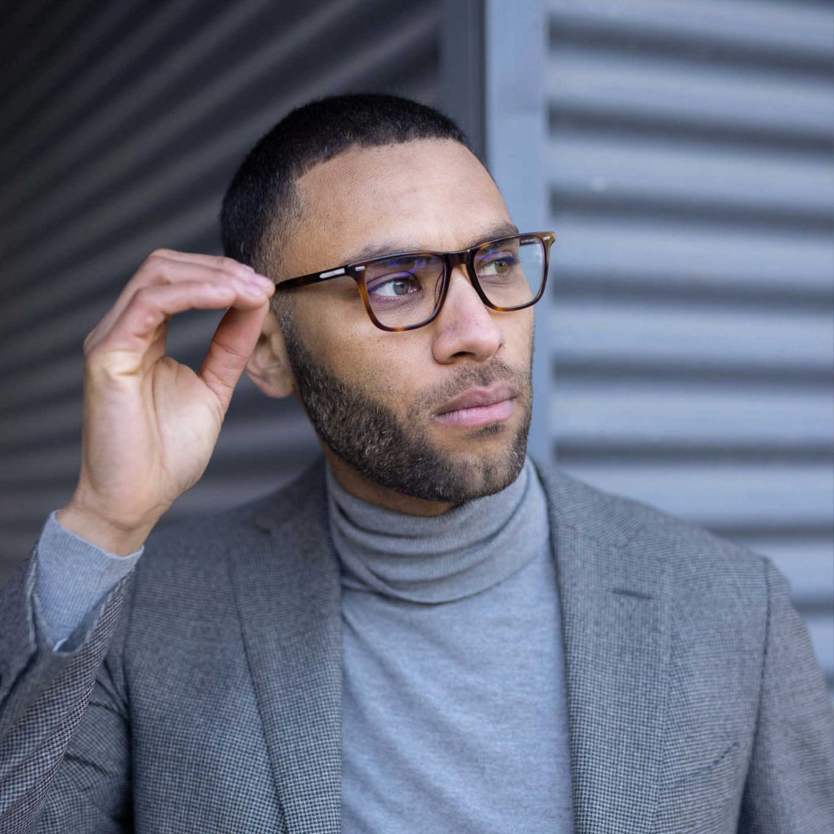Man adjusting glasses against a corrugated metal background
