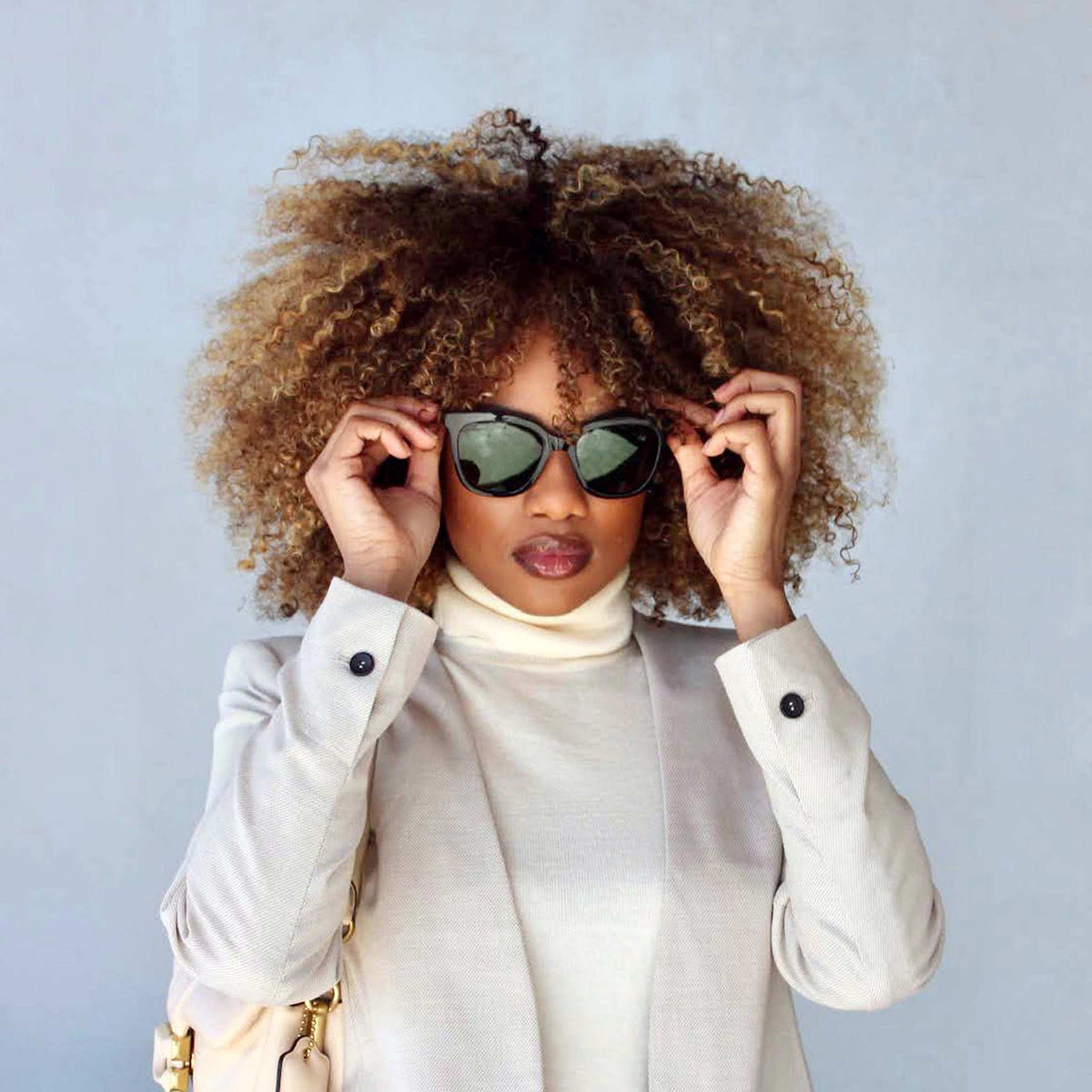Woman wearing sunglasses and a white outfit against a light gray background