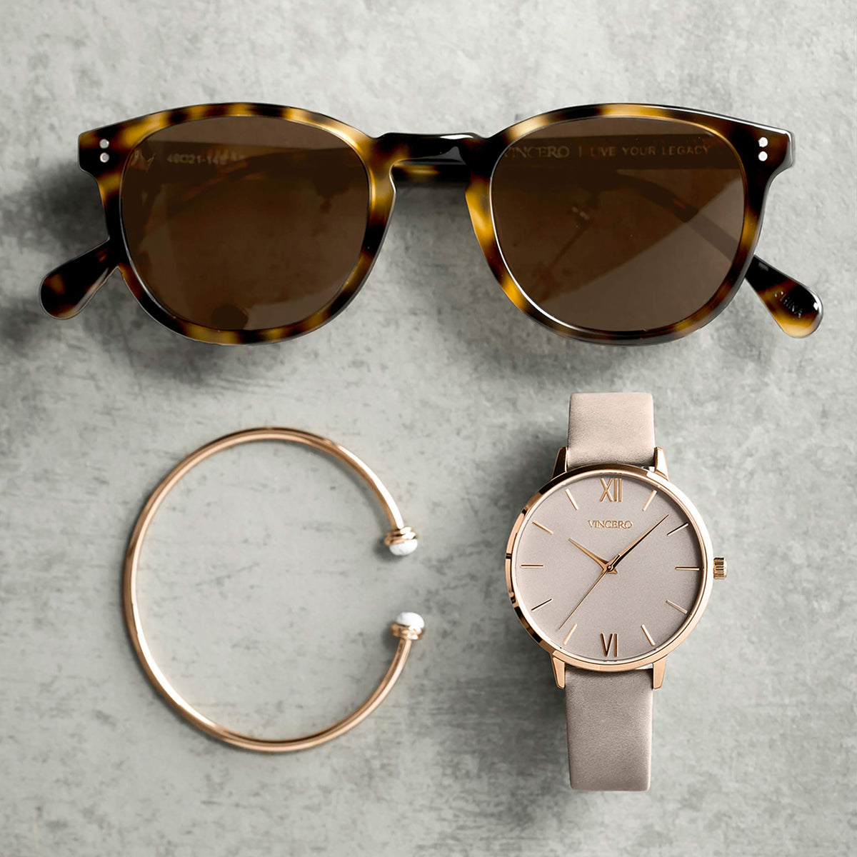 Sunglasses, bracelet, and watch on a gray surface