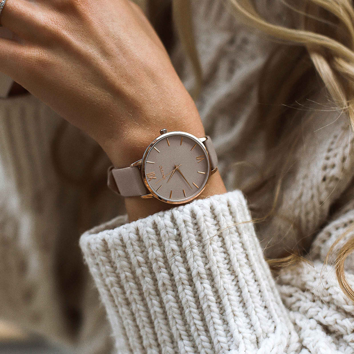 Close-up of a wrist wearing a rose gold watch with a neutral background