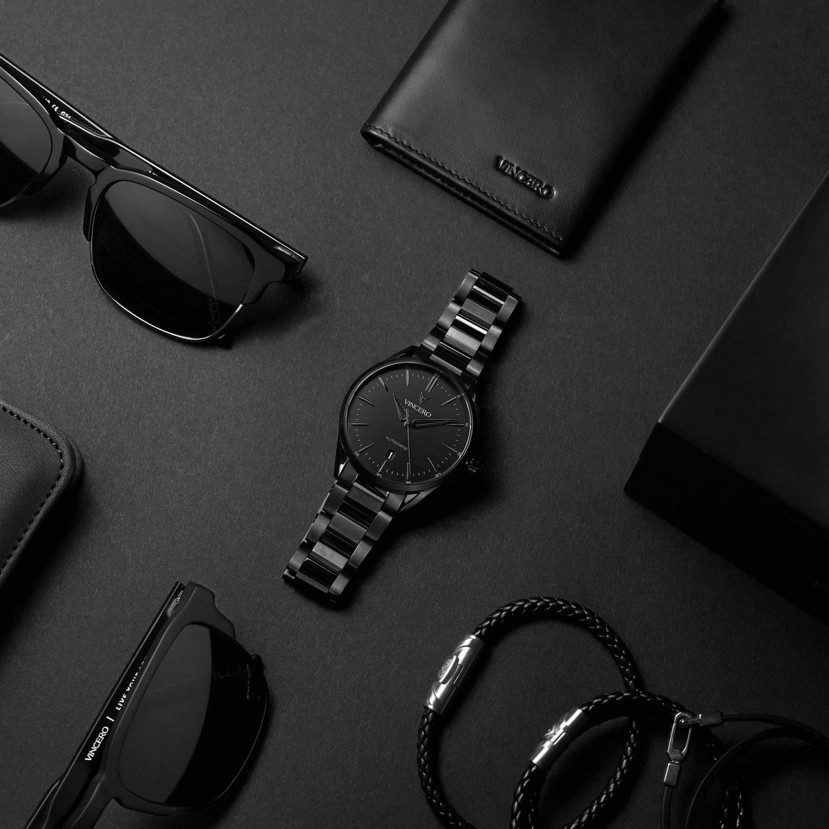 Black watch, sunglasses, and wallet on a dark surface