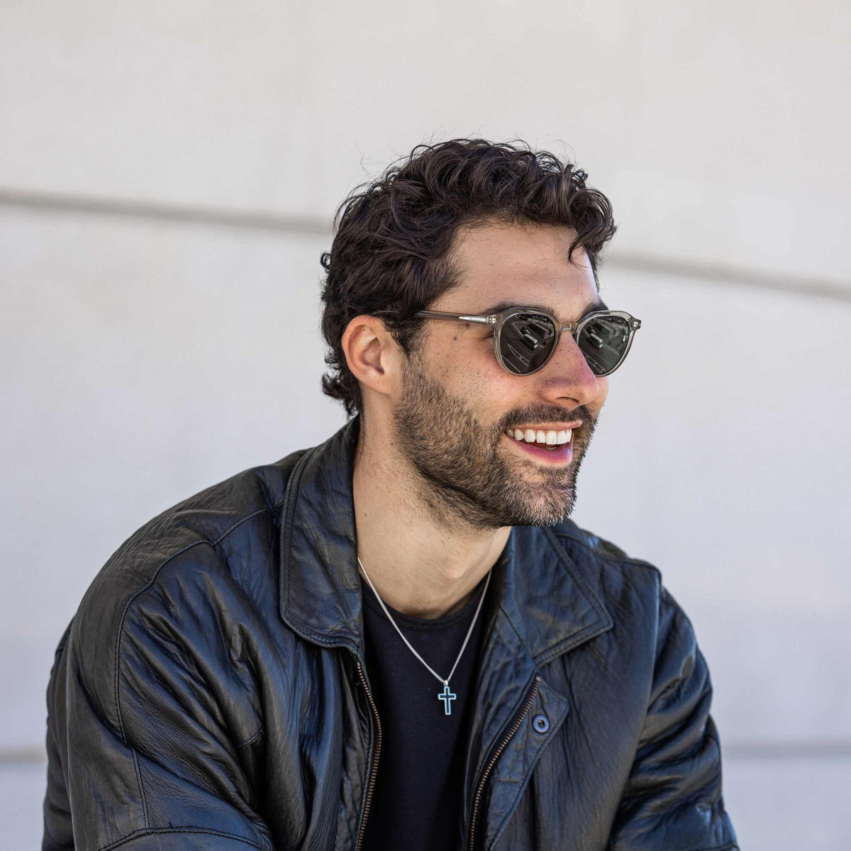 Man wearing sunglasses and a dark jacket against a light background