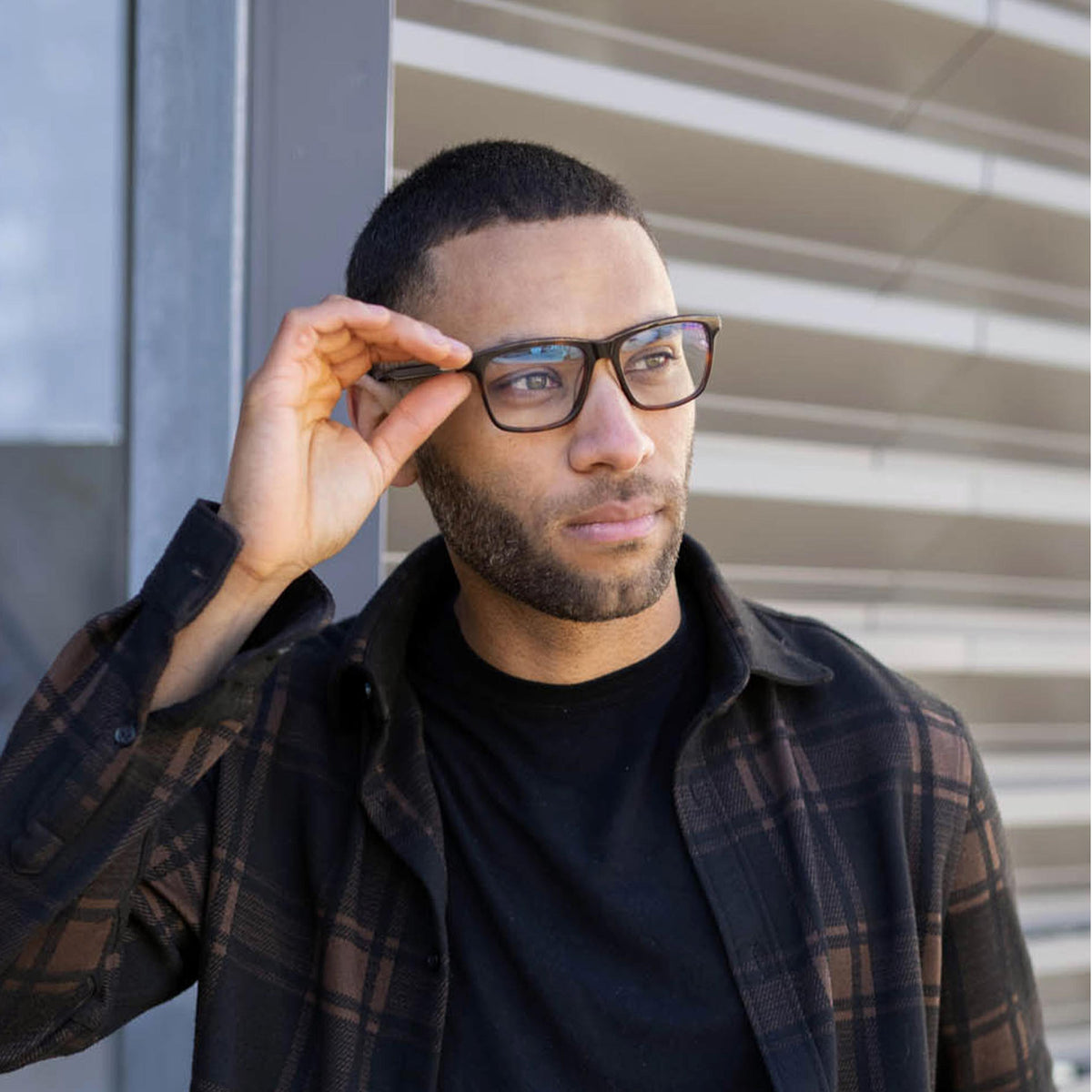 Man adjusting glasses outdoors with a neutral background