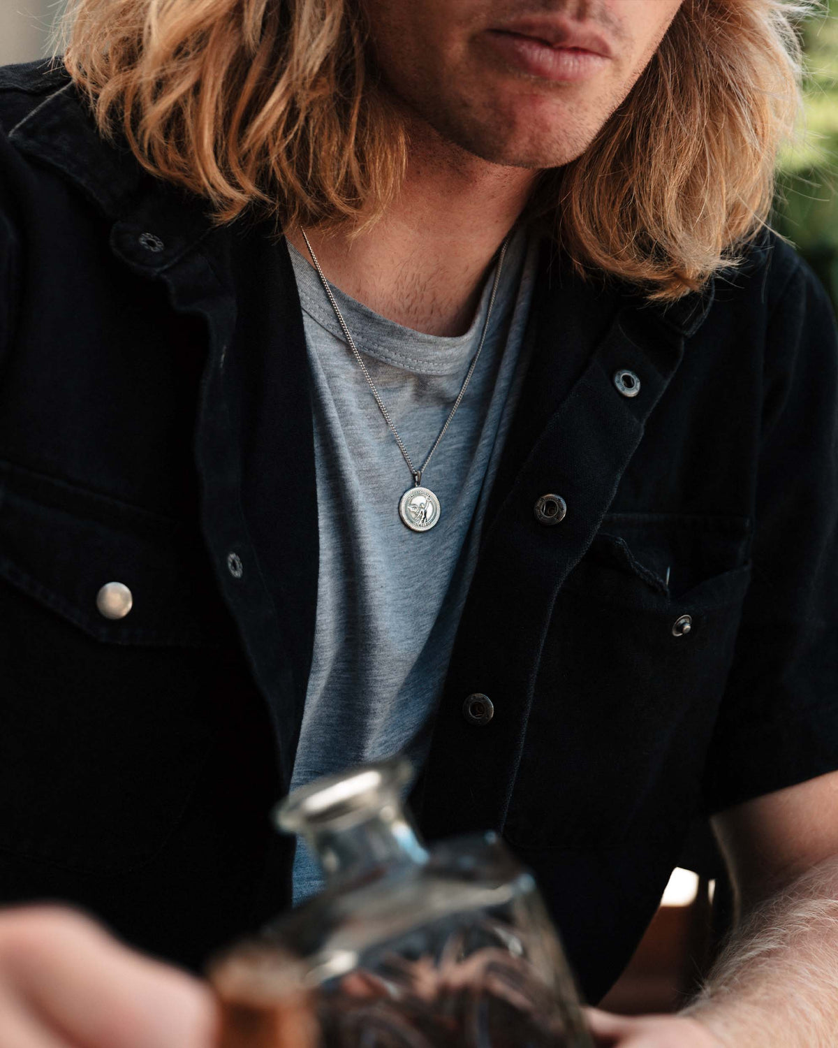 A sterling silver necklace with a round pendant featuring an embossed design, displayed against a white background.